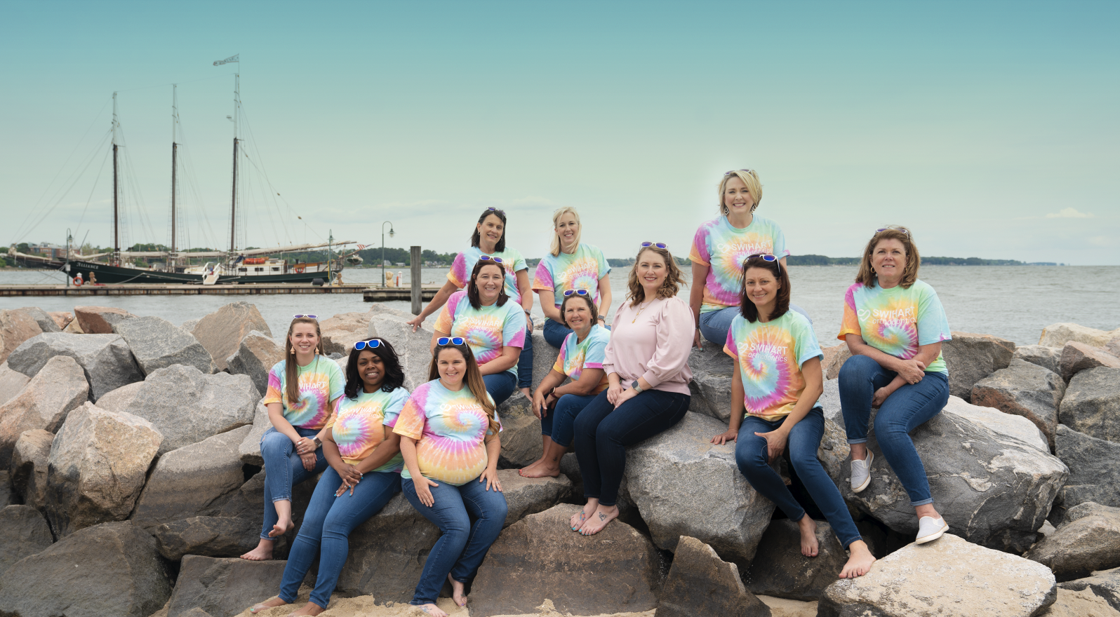 Swihart Orthodnotics Team. Ladies sit on the rocks by the water.